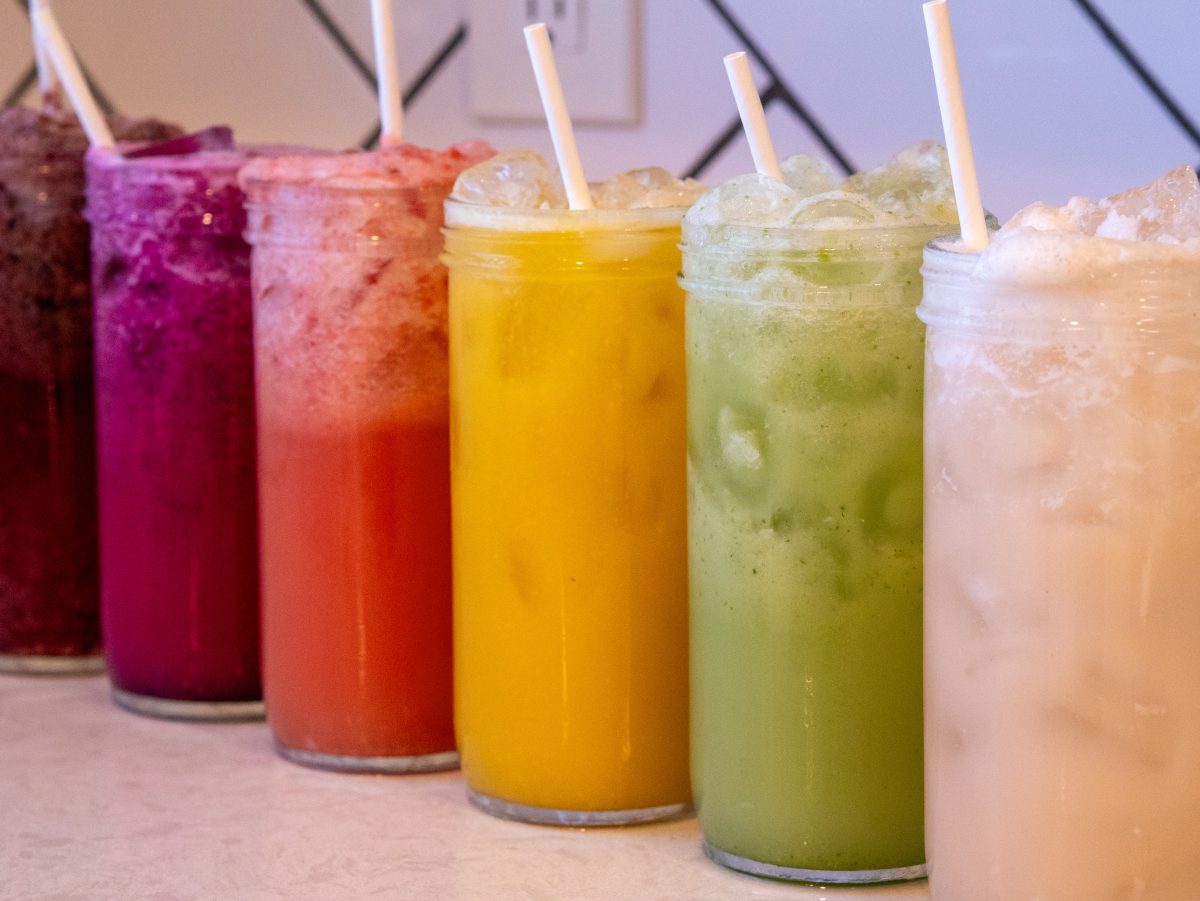 Six colorful homemade Gatorade electrolyte drinks in glass bottles with fresh fruit and coconut water.