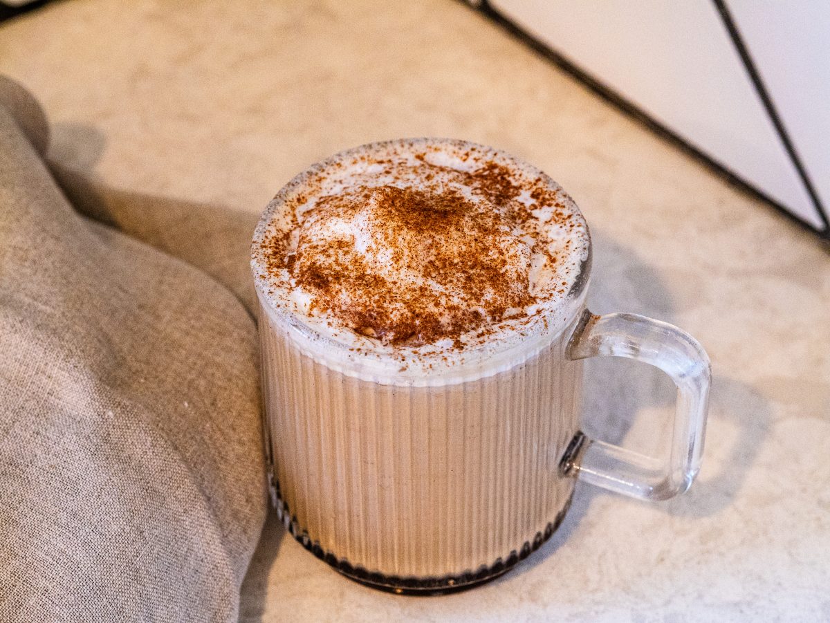 A hot homemade pumpkin spice latte in a clear glass mug topped with vanilla bean whipped cream and dusted with ground cinnamon.