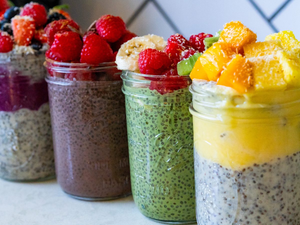 Five healthy chia pudding variations in glass jars, featuring classic, matcha, mango pineapple parfait, mixed berry, and Mexican chocolate.