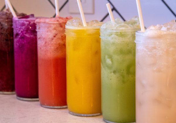 Six colorful homemade Gatorade electrolyte drinks in glass bottles with fresh fruit and coconut water.